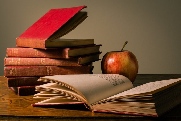 Pile de livres scolaires, livre ouvert et pomme sur un bureau, illustration des révisions par matière pour le brevet des collèges